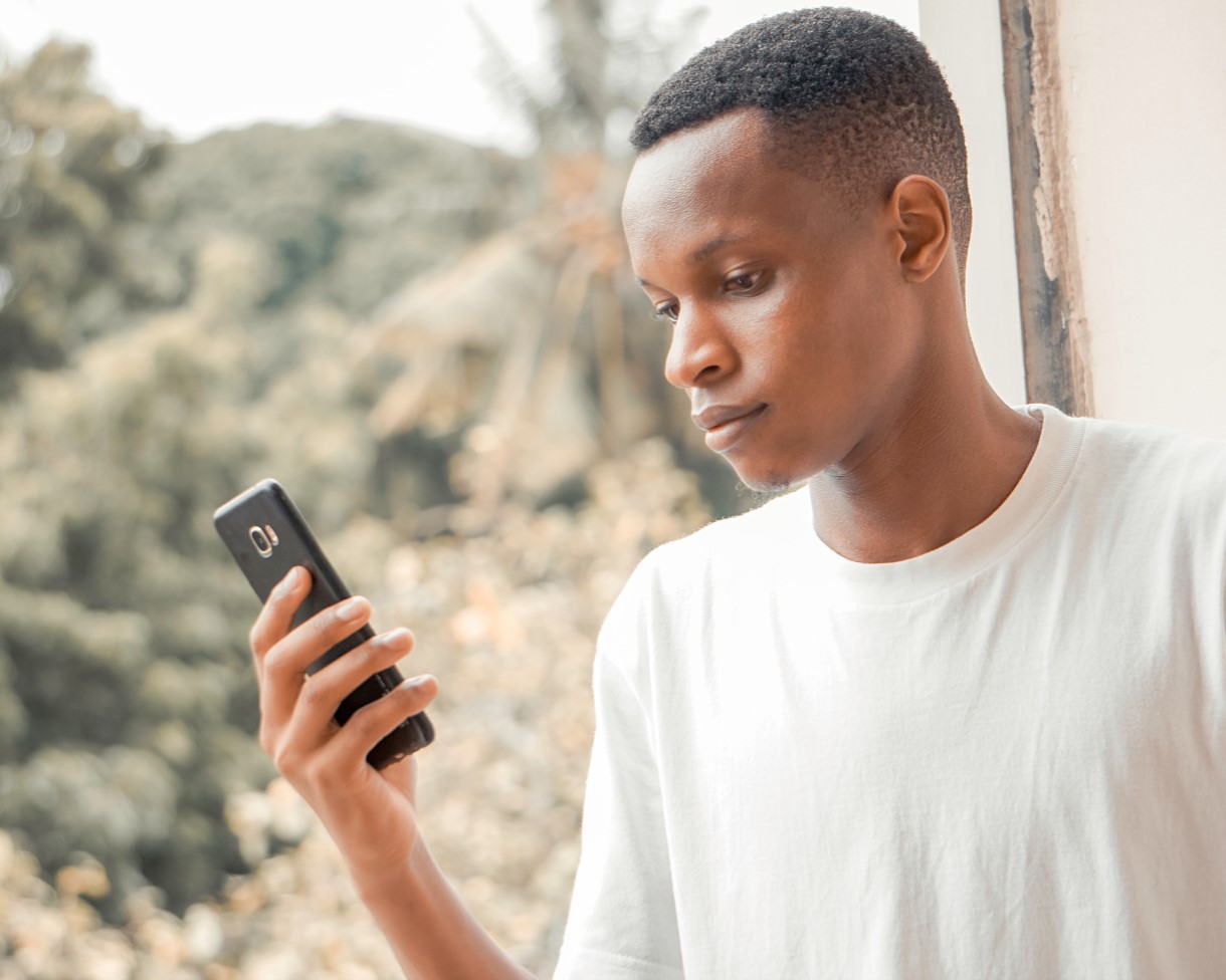 A black man in white t-shirt looks at his phone